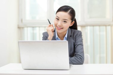 Genç bir kadın dizüstü bilgisayarın önünde oturuyor.