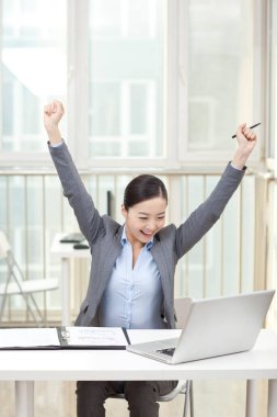 Genç bir kadın dizüstü bilgisayarın önünde oturuyor.