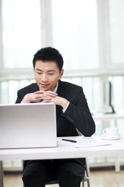 İşadamı portresi oturuyor ve dizüstü bilgisayara bakıyor.