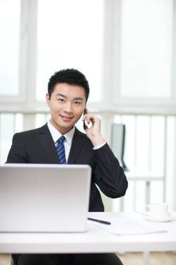 Masada oturan ve cep telefonu kullanan iş adamının portresi.