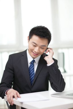 Masada oturan ve cep telefonu kullanan iş adamının portresi.