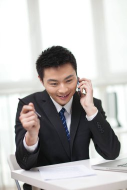 Masada oturan ve cep telefonu kullanan iş adamının portresi.