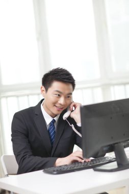 İş adamının portresi bilgisayar başında oturuyor, telefonda konuşuyor.