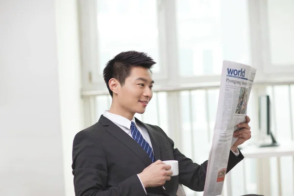 Portrait of businessman holding coffee cup,looking at newspaper