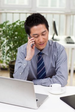 Ofiste bilgisayar ve telefon kullanan bir iş adamı.