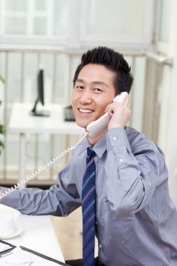 Ofiste bilgisayar ve telefon kullanan bir iş adamı.