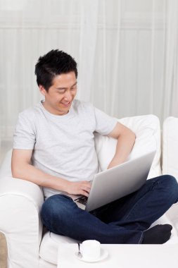 Kanepede dizüstü bilgisayar kullanan neşeli bir iş adamı.