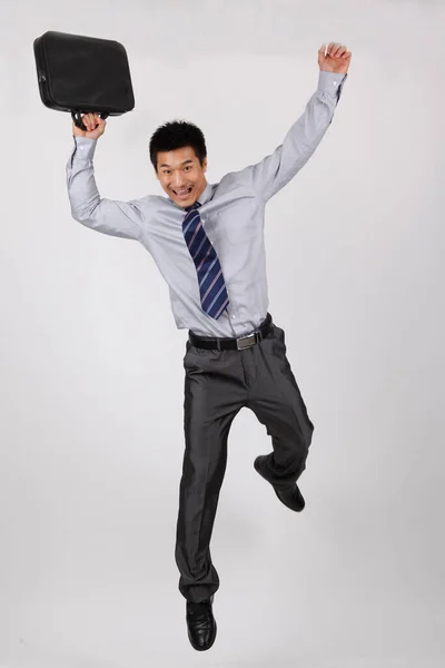 ブリーフケースを持って飛び跳ねる若いビジネスマン — ストック写真