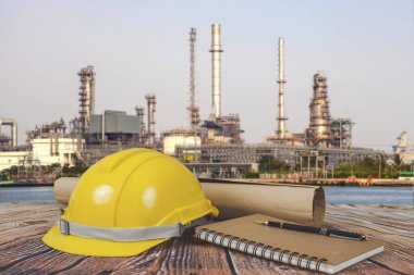 Emanet kask ve tablo üzerinde bulanık petrol rafinerisi arka plan üzerinde kitap.