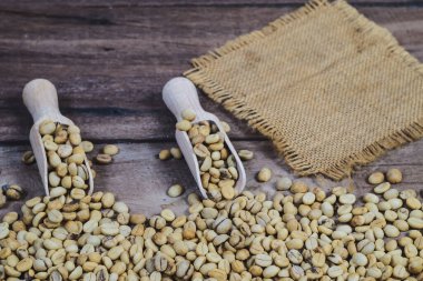 Tahta masadaki kaşık içinde organik çiğ kahve çekirdekleri..