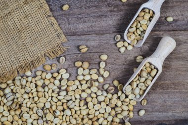 Tahta masadaki kaşık içinde organik çiğ kahve çekirdekleri..