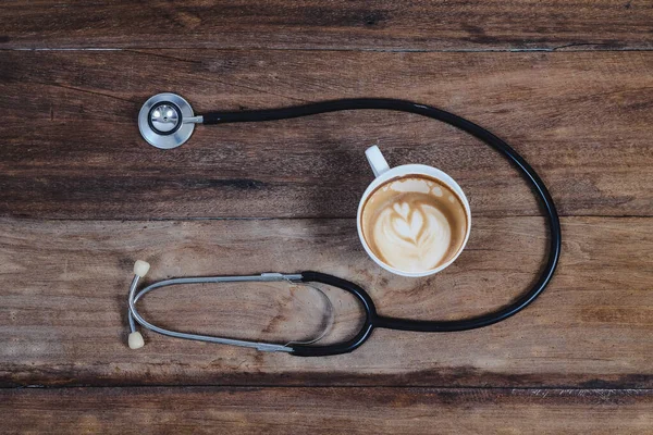 black Stethoscope and late art coffee on wood table.