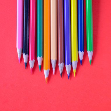 Kırmızı arkaplanda parlak renkli kalemler.