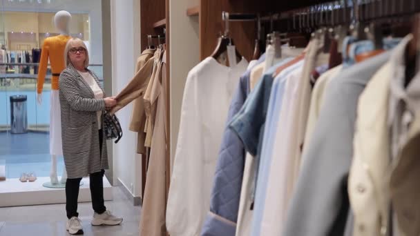 Vrouw kiest kleren in een modewinkel. Een kleine boetiek dameskleding. — Stockvideo