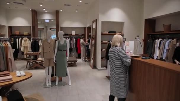 Mulher escolhe roupas em uma loja de moda. Uma pequena boutique de roupas femininas . — Vídeo de Stock