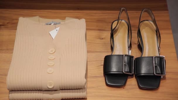 Zwarte damesschoenen, trui, leren rok en pullovers liggen op de planken. — Stockvideo