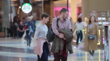 Geniş bir ticaret merkezi, farklı yaş ve cinsiyetlerden insanlar alışverişe gidiyor.