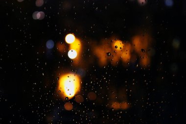 Pencereye ve şehrin gece ışıklarına yağmur yağıyor..