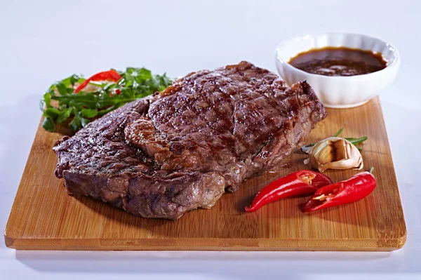 Sappige heerlijke medium gebakken vlees steak op een houten snijplank, met peper, knoflook, kruiden en tomatensaus. Steak voor een restaurant op een witte achtergrond — Stockfoto