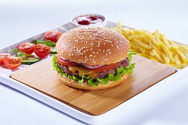 Fransız kızarmış patates kızartması, sebze ve ketçap ile ahşap kesme tahtası üzerinde sulu lezzetli hamburger. Beyaz arka plan ve beyaz servis tepsisi üzerinde yalıtılmış kompozisyon.