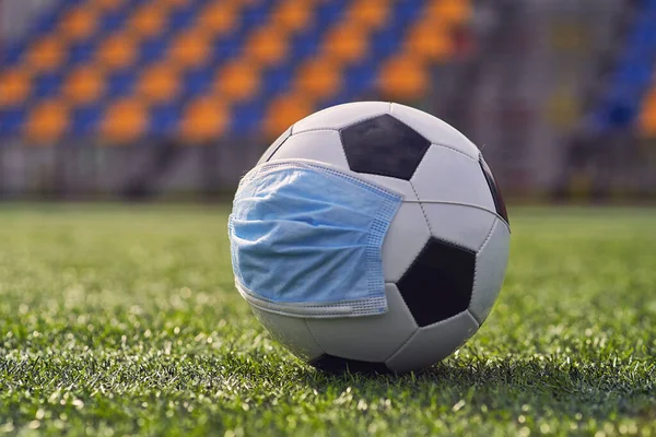 Black and White Soccer Ball In  Medical Mask On  Background of  Empty Seats of  Stadium. Football Competitions During Quarantine Time. COVID-19 Concept