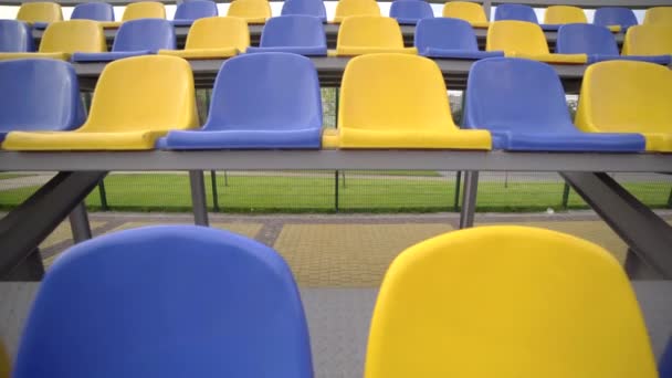 スタジアムの空のプラスチックシート 観客もファンもいないフットボールスタジアム トリビューンの黄色と青の席の列 — ストック動画