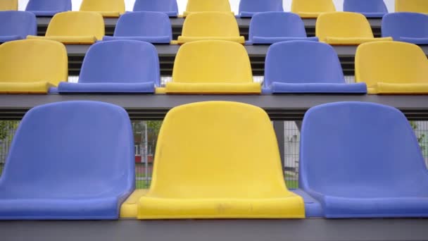 スタジアムのプラスチックシートの空の行 観客やファンのいないスポーツアリーナのトリビューンの黄色と青の席 — ストック動画