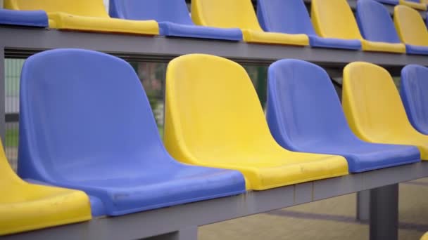 スタジアムのプラスチックシートの空の行 観客やファンのいないスポーツアリーナのトリビューンの黄色と青の席 — ストック動画
