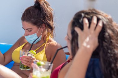 İki genç kız güneşleniyor ve terasta plastik bir havuzda mojito içiyor.