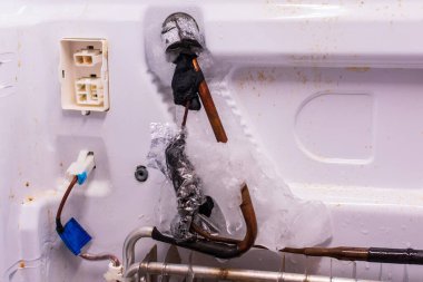 Refrigerator repair. Freezer compartment back panel removed. Evaporator coils with a frozen thermostat. clipart