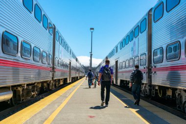 Gündüz vakti, San Francisco, Kaliforniya, ABD - 2019 sayılı banliyö tren istasyonundaki Caltrain vagonuna binmek üzere açık hava tren platformunda yürüyen yolcular.