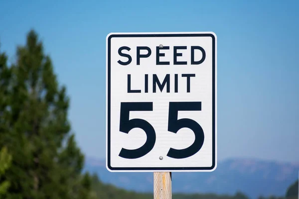 Fifty-five mph speed limit sign on highway. Speed zone traffic sign against blurred tree landscape and blue sky.