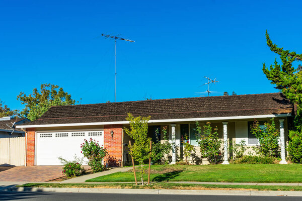 Exterior view of traditional ranch style single family detached home with a long, low-rising roof in an older established residential neighborhood.