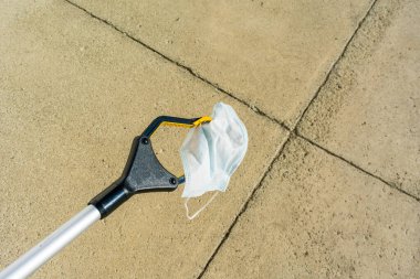 Uzatıcı beton geçide karşı kullanılmış tek kullanımlık bir cerrahi maske tutuyor..