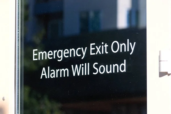 Emergency exit only, alarm will sound sign on the glass exit door leading to safety.