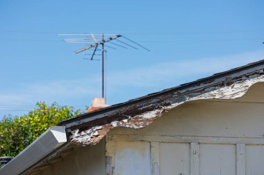 Açık mavi gökyüzünün altında soyulmuş boyası ve açıkta duran ahşabı olan eski mesken çatısı, dış çürümeyi, yıpranmayı ve yenileme ve onarım ihtiyacını vurguluyor.