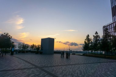 New Jersey 'de günbatımı. Asfaltlı meydanın ortasında duran bir grup insan silueti