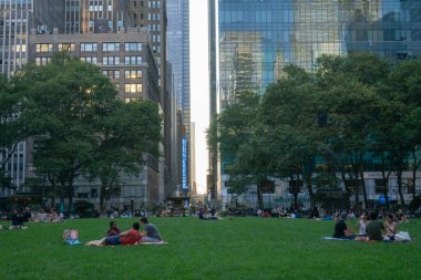 İnsanlar çimenlerde oturup Bryant Park 'ta piknik yapıyor ve havanın tadını çıkarıyor. Arka planda gökdelenler