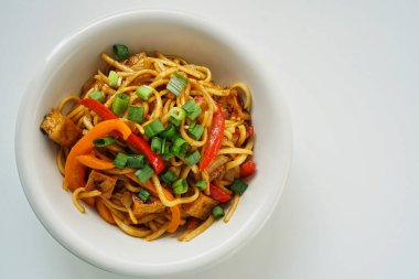 Kızarmış tofu ve sebzelerin beyaz bir tabakta ve beyaz arka planda üst görüntüsü