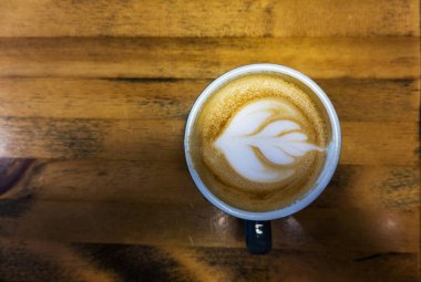 Ahşap arka planda sanatsal çiçek şekilli kahvenin en üst görüntüsü.