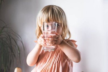 Bir bardak suyla küçük tatlı bir kız. Sağlıklı yaşam tarzı kavramı.