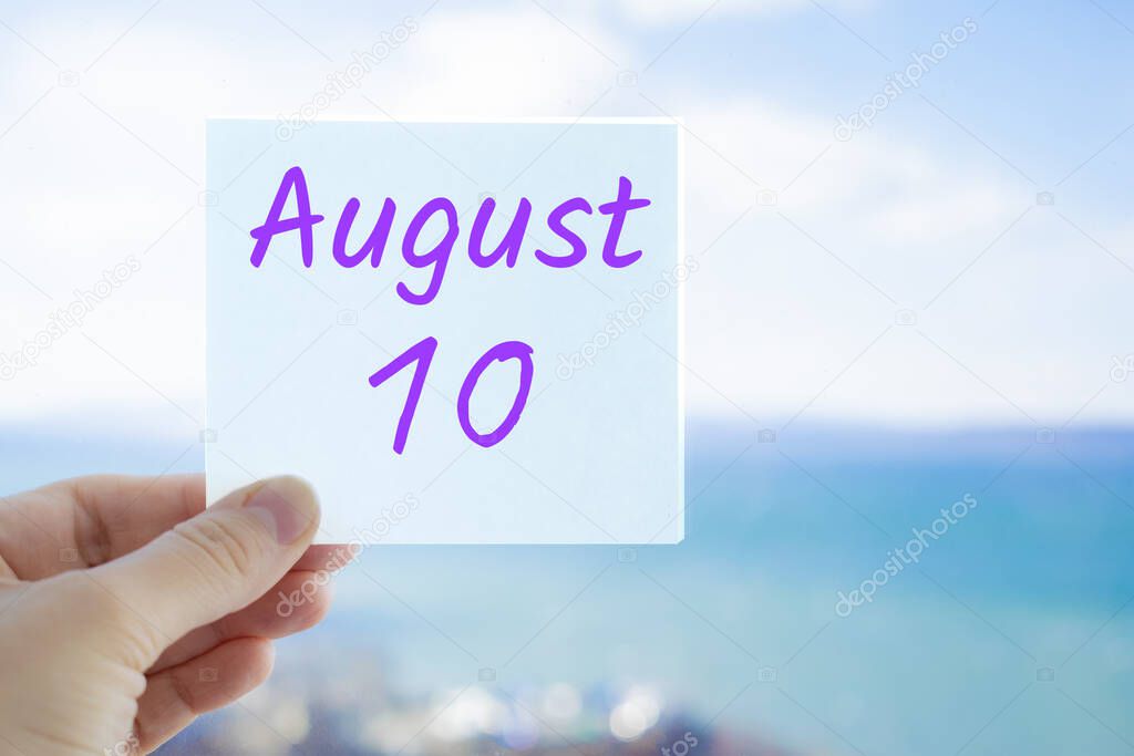 August 10th. Hand holding sticker with text August 10 on the blurred background of the sea and sky. Copy space for text. Month in calendar concept.