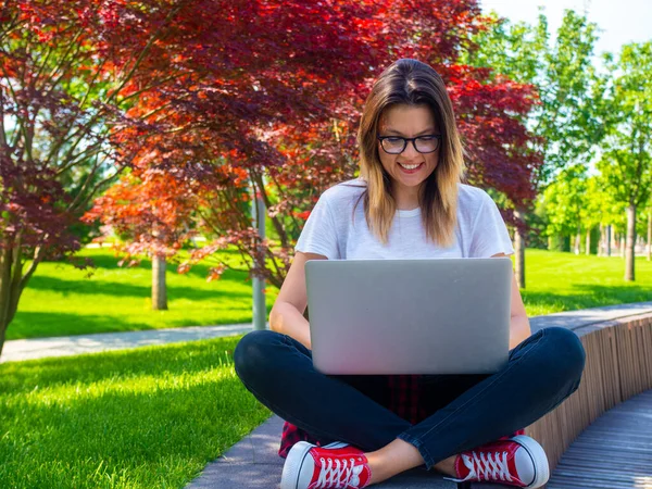 Женщина сидит со скрещенными ногами с ноутбуком на улице. Концепция онлайн образования — стоковое фото