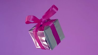 Kırmızı kurdeleli hediye kutusu neon mor arka planda dönüyor. 360 derece rotatio