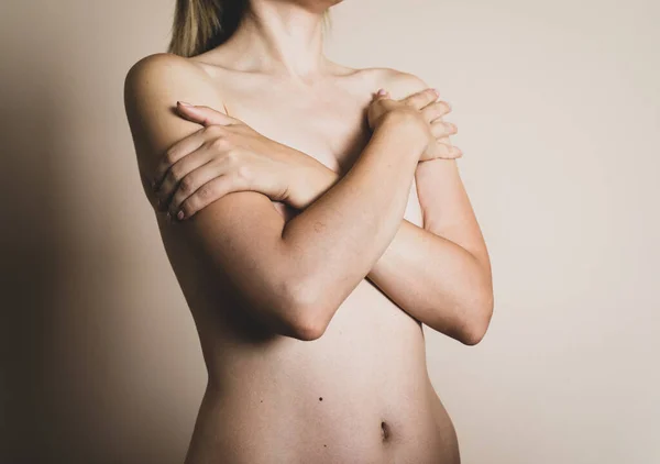 A young naked blonde woman crossed her arms on her chest on a beige background — Stock Photo, Image