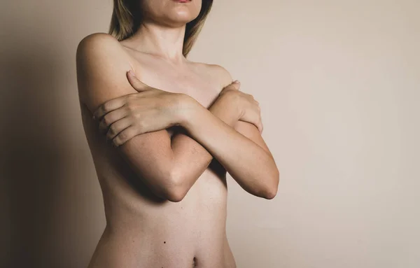 A young naked blonde woman crossed her arms on her chest on a beige background — Stock Photo, Image