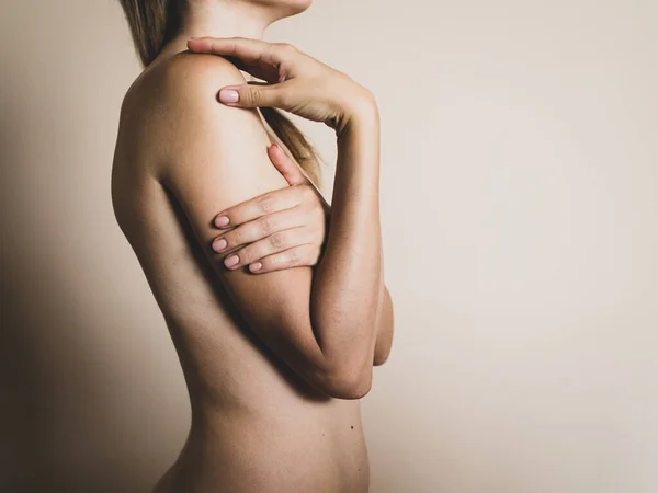 Une jeune femme blonde nue croise les bras sur sa poitrine sur un fond beige — Photo