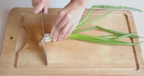 Kvinnors händer skurna med kniv fjäder lök bunt på trä skärbräda — Stockvideo