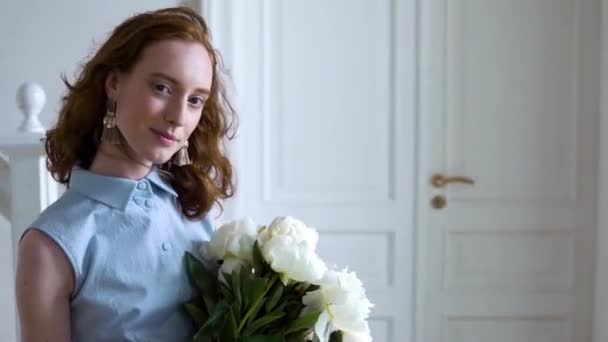 Close up portrait of beautiful red haired girl sniffs a big bush of white peonies — Stock Video