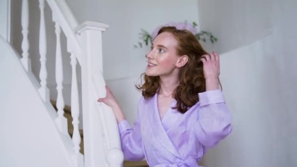 Alegre chica positiva posando para la cámara en un traje púrpura de pie en una escalera blanca — Vídeos de Stock